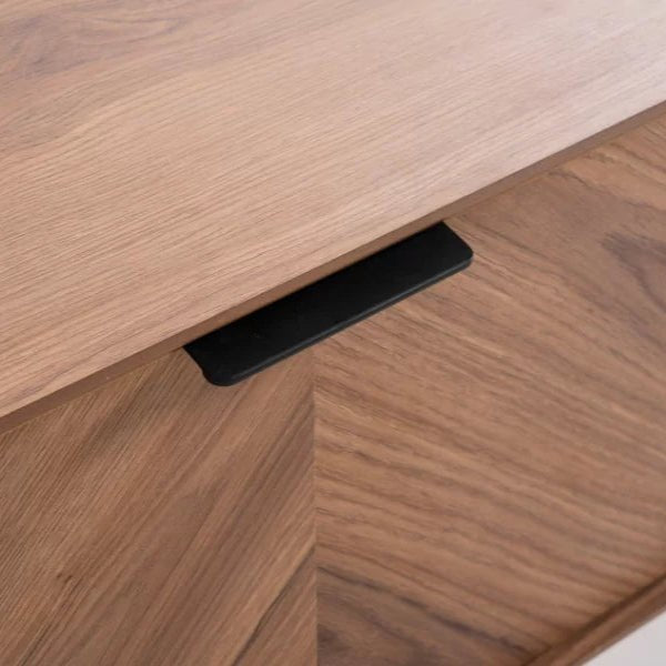 Foster TV Unit 200cm. Extreme close-up of the light wood TV unit, focusing on the seamless integration of the top surface and the cabinet door featuring a prominent chevron wood grain pattern. The image highlights the minimalist black recessed pull handle, emphasizing the sleek, modern design detail.