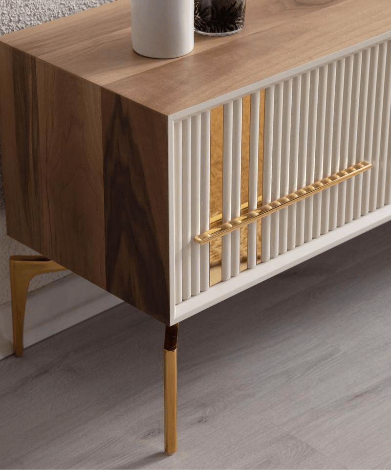 Lincoln Wooden Tv Unit cream 200cm. Close-up detail of one end of the media console, highlighting the vertical ribbed texture of the cream cabinet door, the gold linear accent and handle, the natural wood side panel, and the glossy gold angled metal legs.
