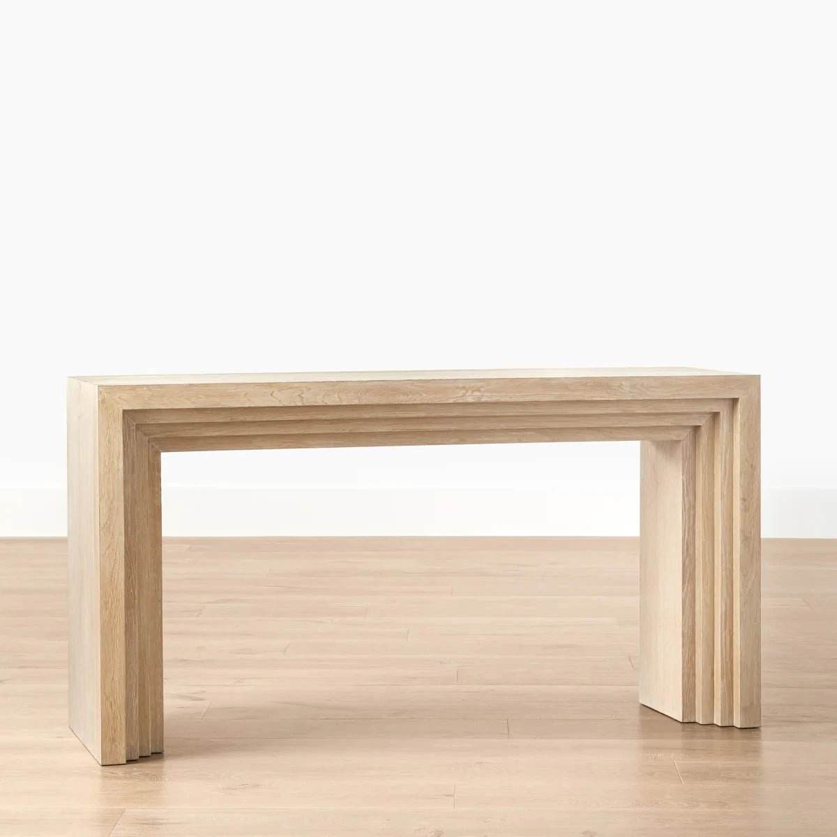 A sleek Meridian Console Table made of engineered wood with a natural oak finish, featuring a waterfall design, placed on a wooden floor against a white background.