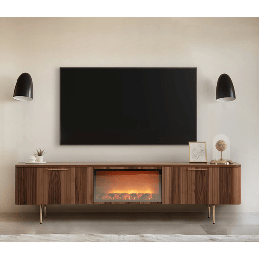 Asta Wooden Fire TV Unit 200cm. Long, mid-century modern style TV stand made of warm brown walnut wood, featuring two slatted storage cabinets on the sides and an integrated central electric fireplace insert with glowing logs. The unit is supported by slender brass legs and is shown beneath a large wall-mounted TV in a stylish living room setup, providing both storage and ambient.