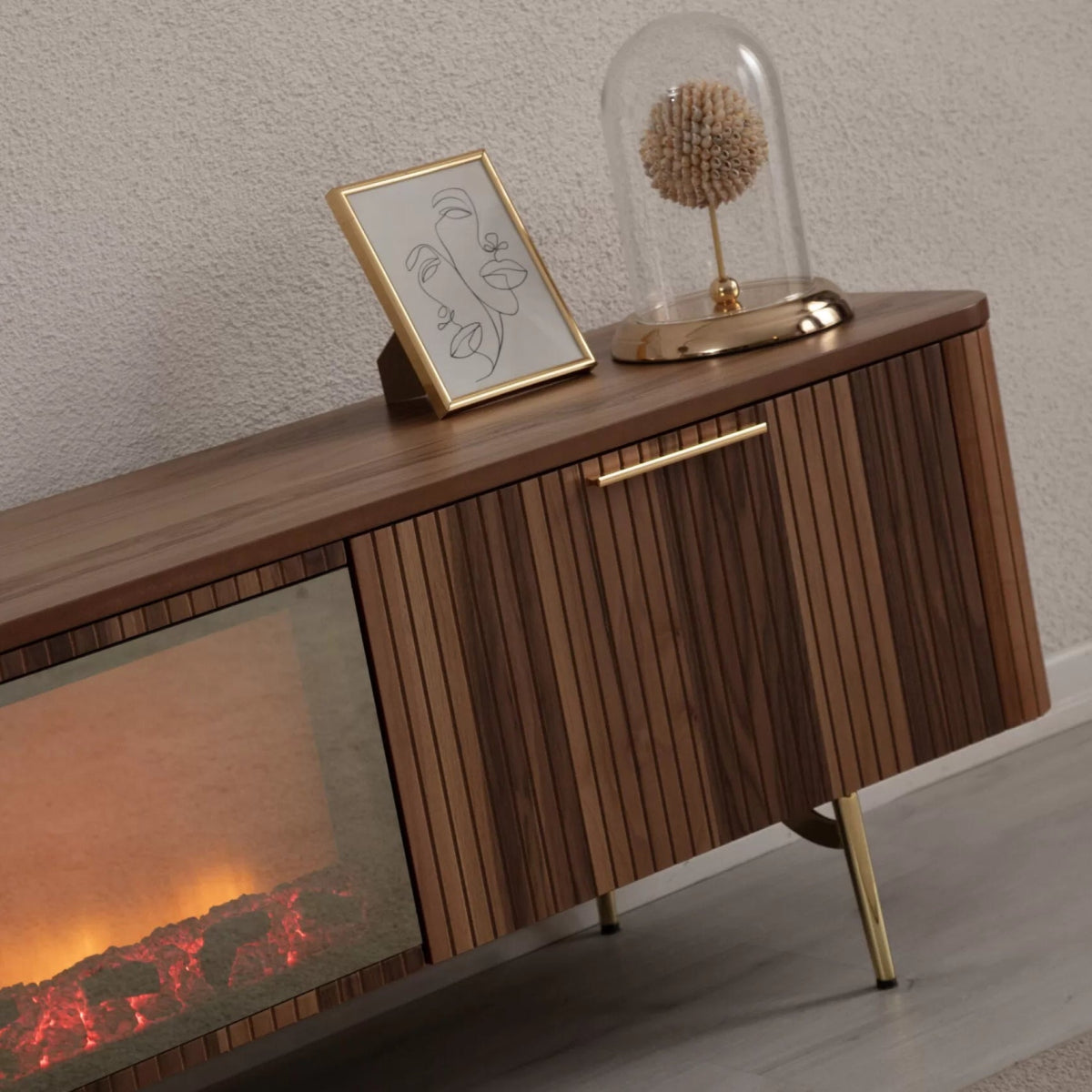 Asta Wooden Fire TV Unit 200cm. Close-up, angled view of the right end of the TV unit, showing the warm brown walnut wood finish, rounded edges, slatted cabinet door, and brass handle and leg. The integrated electric fireplace display insert with a glowing log effect is visible on the left, demonstrating the unit's elegant design and warming effect.