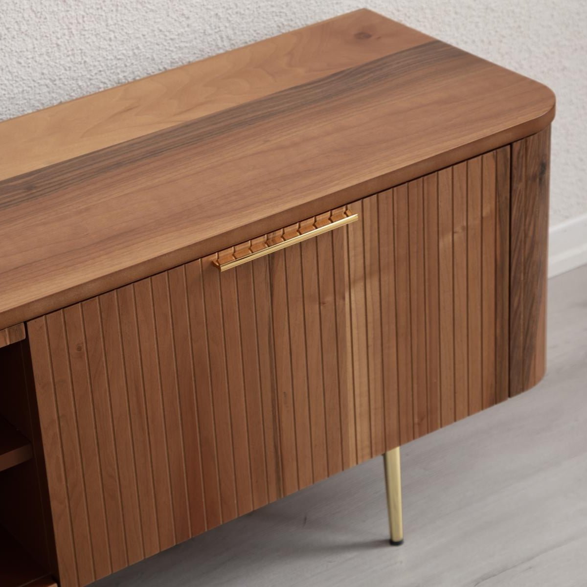 Asta Wooden TV Unit 200cm. Close-up view of the side cabinet, showing the rich brown walnut wood top with rounded edges and the vertical slatted/ribbed wood paneling on the door. Features a long, horizontal brass-toned handle and a thin brass leg, highlighting its elegant, mid-century modern design.
