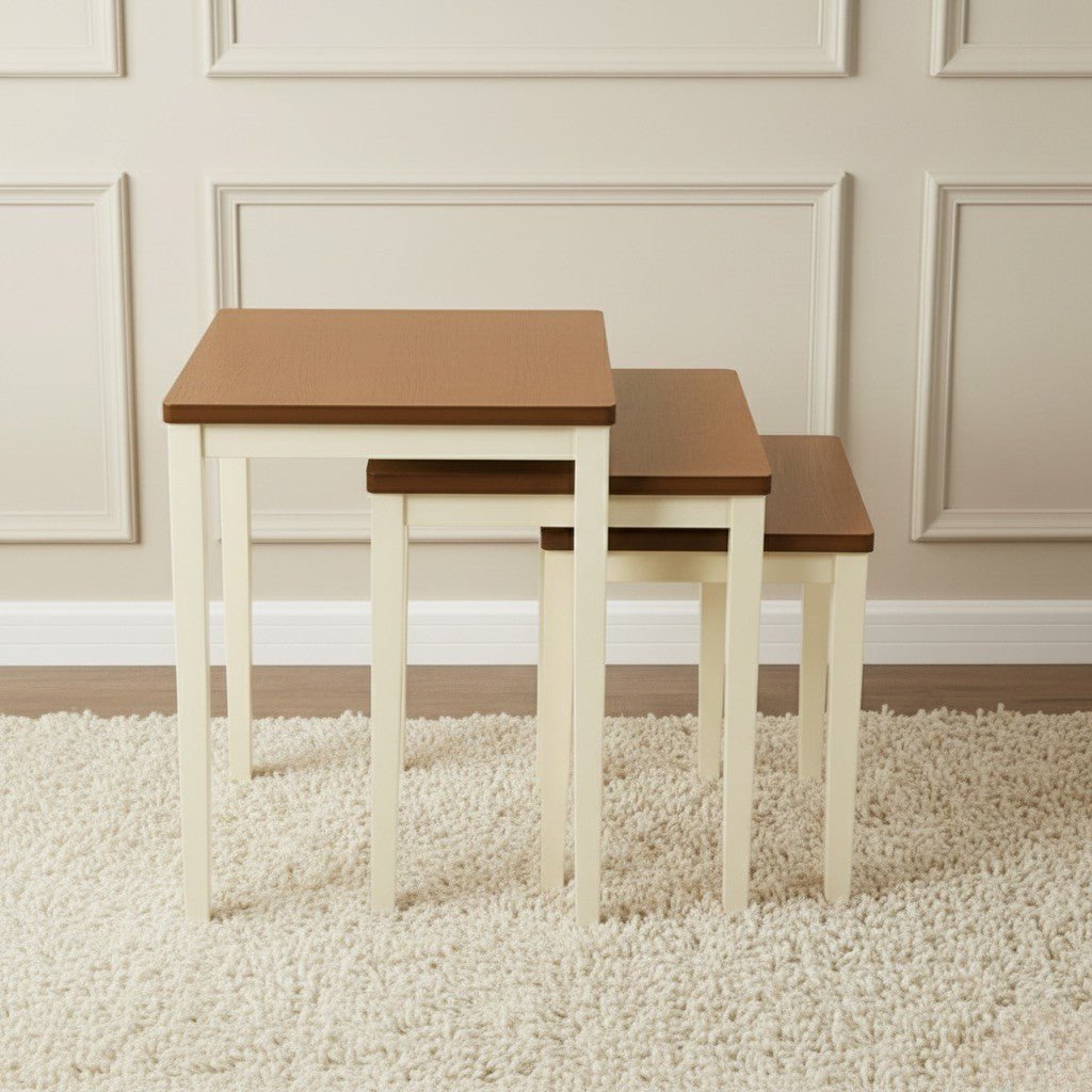 Set of three nesting tables with wooden tops and white bases on a carpeted floor.