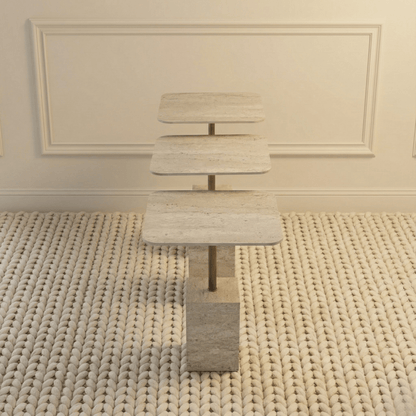 Travertine nesting tables on a textured rug against a wall with decorative molding.