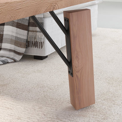 Close-up of a wooden table leg support with a rectangular wood post and black metal bracket, shown in a real interior setting on a light rug beside a sofa with a plaid throw.