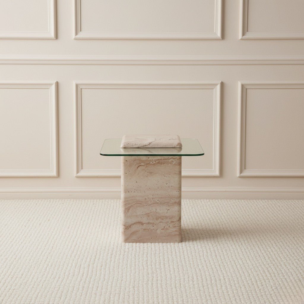 Glass table with travertine stone base against a beige paneled wall