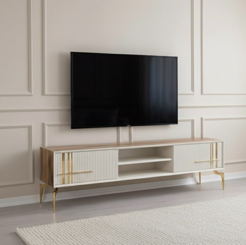 Lincoln Wooden Tv Unit Cream 200cm. Wide media console with a light wood frame and cream cabinet fronts featuring vertical ribbed texture, gold linear accents and handles, a central open shelving area, and supported by glossy gold angled metal legs beneath a wall-mounted TV.

