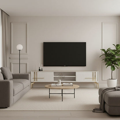 Lincoln Wooden Tv Unit cream 200cm. Full view of a minimal living room featuring the wide cream media console with ribbed cabinets, gold linear accents and handles, and gold angled legs, positioned beneath a wall-mounted TV between a grey sofa and a potted plant.