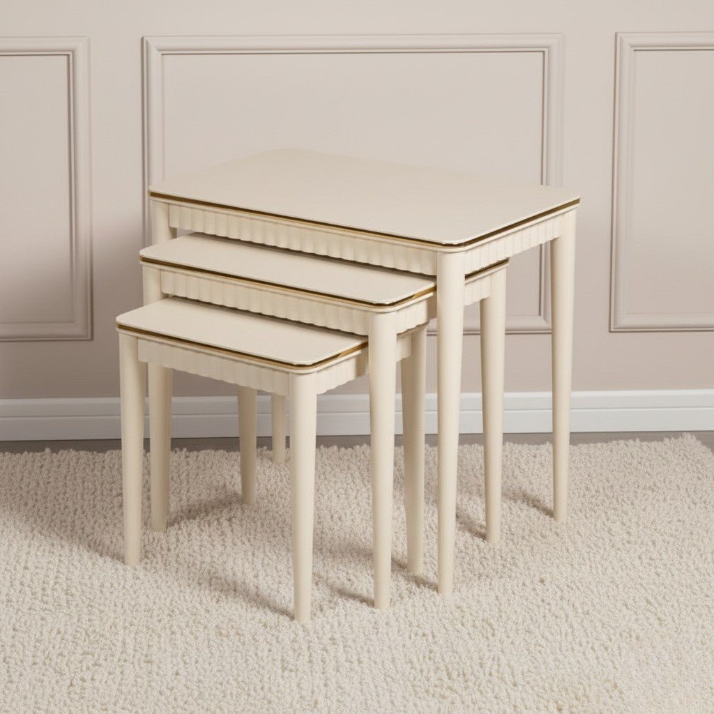 Set of three beige nesting tables with gold trim on a light carpeted floor.