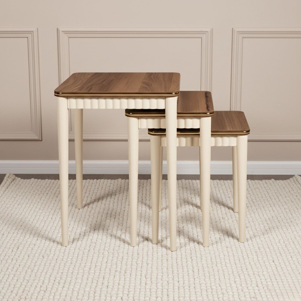 Set of three wooden nesting tables with a white base against a beige wall.
