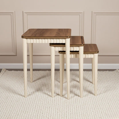 Set of three wooden nesting tables with a white base against a beige wall.