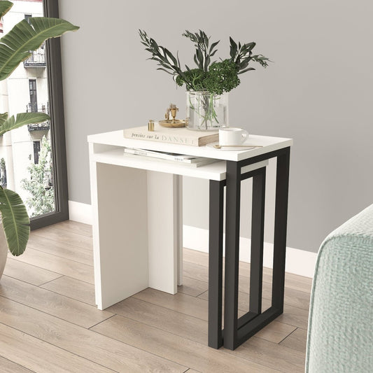 A modern nesting side table set with a white top and black geometric frame legs, styled in a bright room with a vase of greenery and a coffee cup on top.