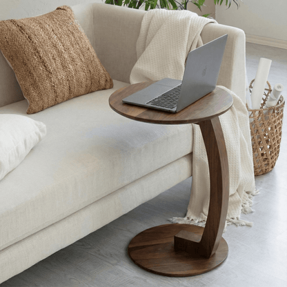 Wooden side table with a laptop on it next to a beige sofa in a living room.