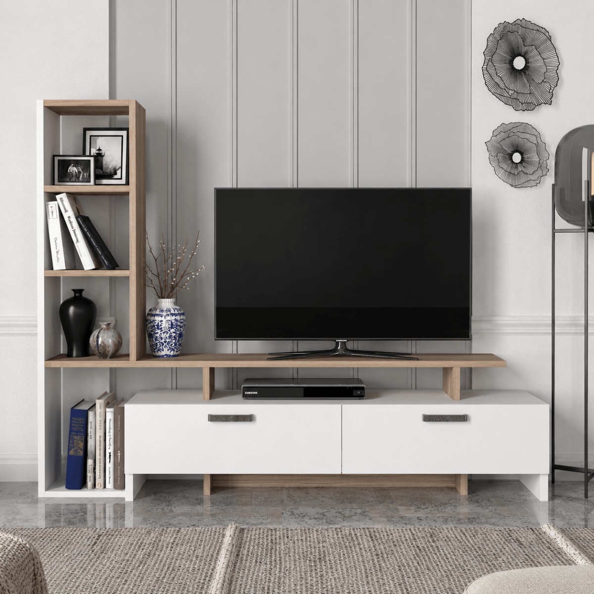 A modern TV stand and shelving unit in a styled living room. The white TV stand with light wood legs holds a black flat-screen TV and a DVD player, while a matching light wood open bookshelf stands to the left with books, frames, and decorative vases.