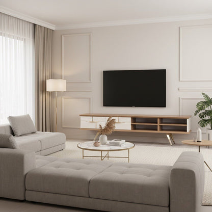Tribe Wooden Tv Unit Cream 200cm. Full view of a bright, neutral living room featuring the wood and cream media console with gold angled legs and open shelving, positioned below a mounted TV. The room includes a large tufted grey sectional sofa and a round marble coffee table.